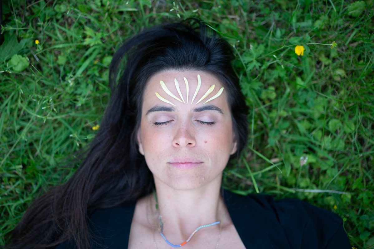 Isadora laying on the grass with flower petals in the head representing the mystical aspect of this New Moon in Pisces